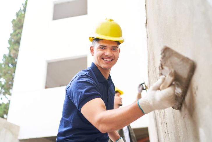 Ein Stuckateur verputzt eine Außenwand eines Hauses