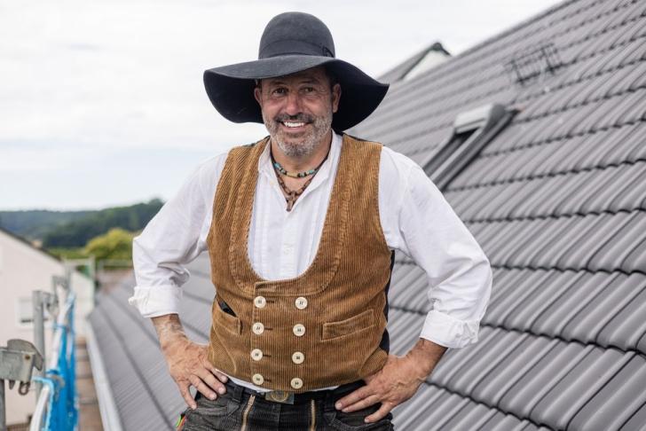 Ein Dachdeckermeister steht auf dem Dach und lächelt in die Kamera